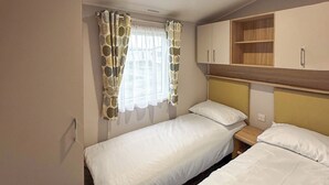 Quarto individual com duas camas, janela com cortinas estampadas, cabeceira de madeira e prateleira embutida.