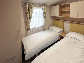 A single bedroom with two beds, a window with patterned curtains, a wooden headboard, and a built-in shelf. - Golf Village 107 - UKC9578 (Mablethorpe)