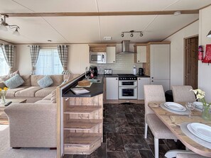 A compact living space with a kitchenette, a dining area, and a sofa. - Oak Village 83 - UKC9580 (Mablethorpe)