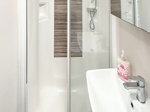 A bathroom with a white sink, a handheld showerhead, and a bottle of soap. - Oak Village 83 - UKC9580 (Mablethorpe)