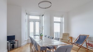 Une pièce spacieuse comprenant une grande table à manger, plusieurs chaises, un téléviseur et un balcon avec vue.
