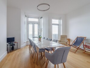 Ein geräumiges Zimmer mit großem Esstisch, mehreren Stühlen, einem Fernseher und einem Balkon mit Aussicht.