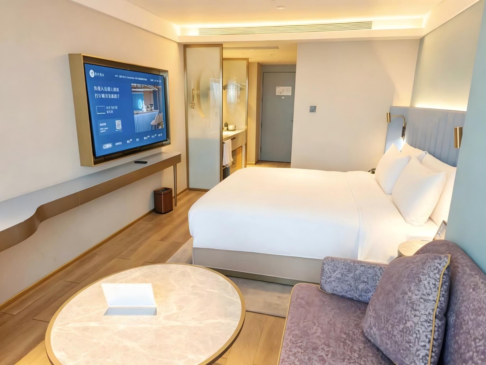 A hotel room with a bed, a TV mounted on the wall, a round table, and a sofa.