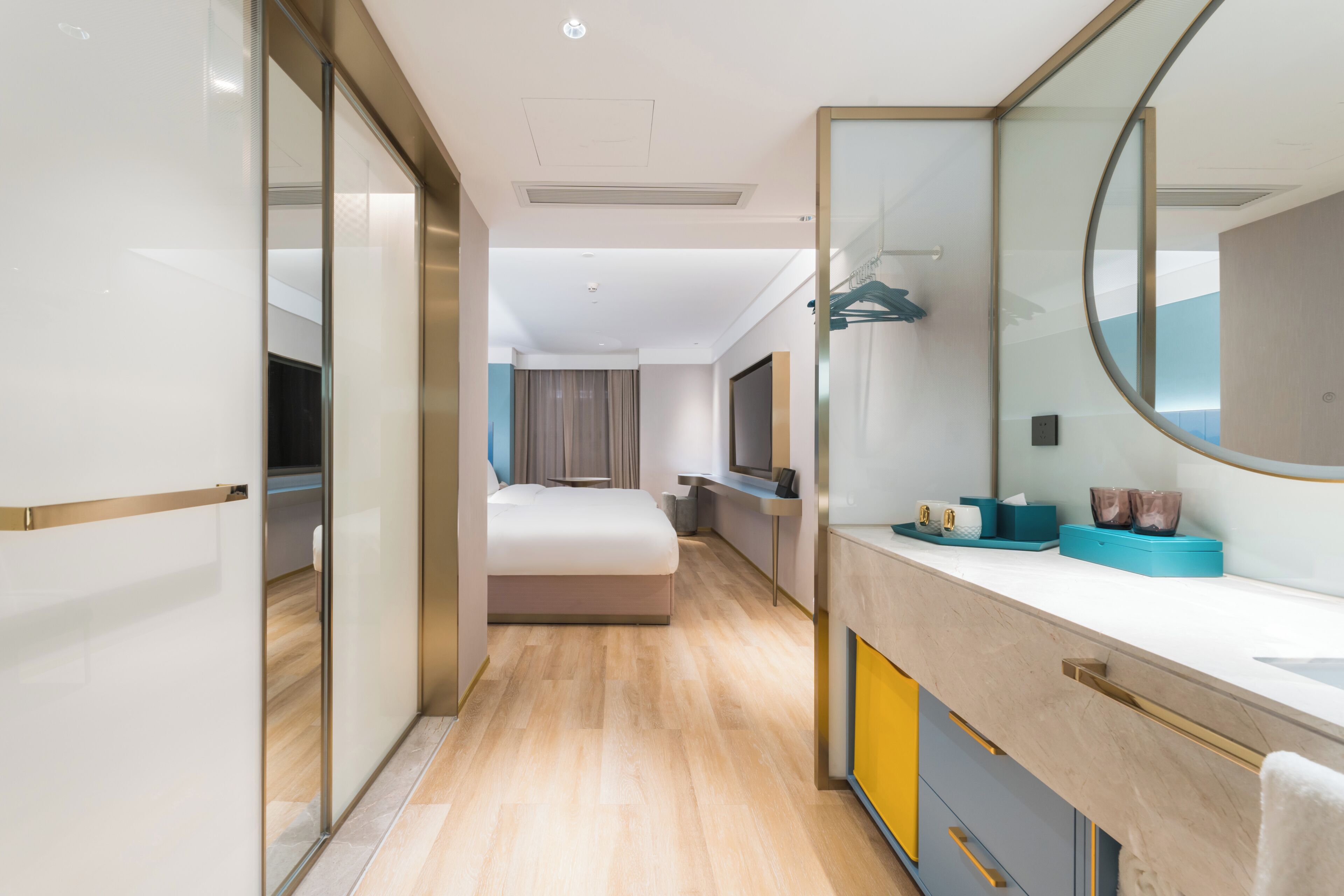 A modern hotel room with a bed, a large mirror, a vanity with toiletries, and a view of the city.