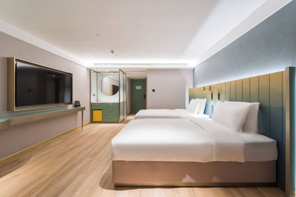 A modern hotel room with a large bed, a TV, a mirror, and a wooden floor.