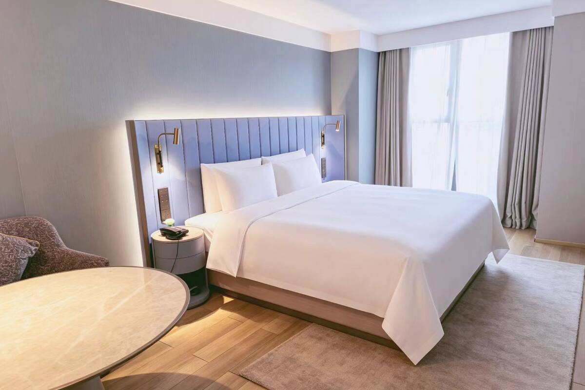 A modern hotel room with a large bed, a round table, and a nightstand.