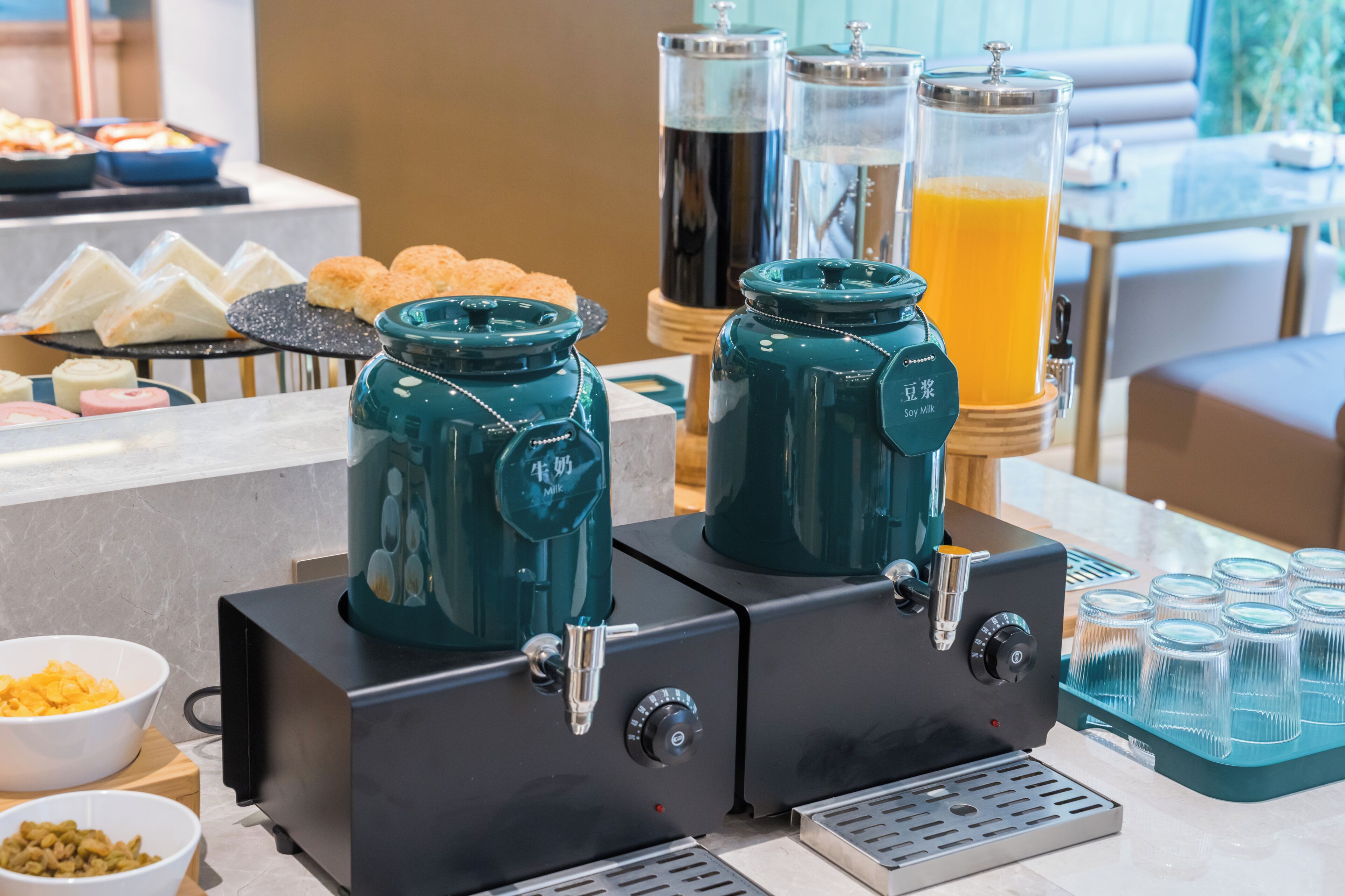 Un buffet de petit-déjeuner avec des machines à café, du lait de soja et des distributeurs de jus d’orange.