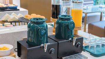 Un buffet de petit-déjeuner avec des machines à café, du lait de soja et des distributeurs de jus d’orange.