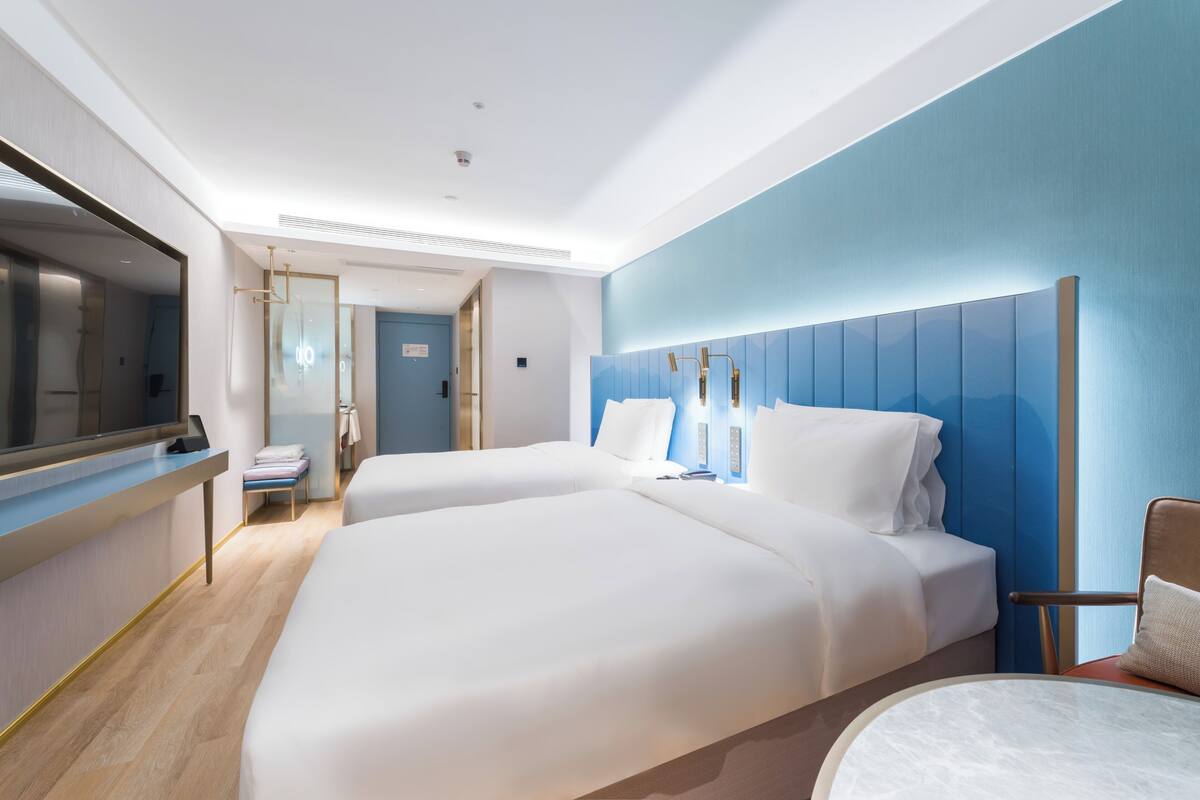 A modern hotel room with two beds, a desk, and a TV.