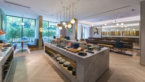 Un moderno vestíbulo de hotel con una zona de bar central, distribuciones de asientos y grandes ventanales con vistas a zonas verdes.