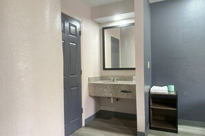 Een badkamer met een donkere deur, een wastafel met granieten blad, een spiegel en een handdoekenplank.