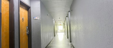 A long, narrow hallway with doors on both sides, a sign indicating room number 222, and a bright light at the end.