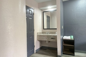 Une salle de bain avec une porte sombre, un lavabo sur un plan de travail en granit, un miroir et une étagère à serviettes.