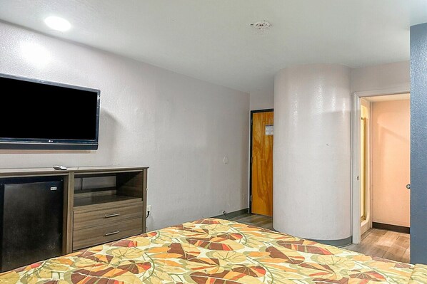 A hotel room with a bed, a TV, a minibar, and a door leading to another room.