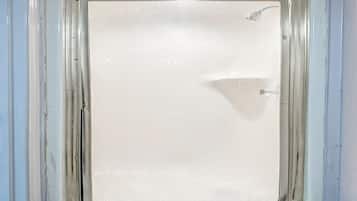 A bathroom with a white shower enclosure, a visible showerhead, and a door handle.