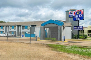 A motel with a blue awning, a fenced parking area, and a sign advertising low rates and All-in-one rooms.