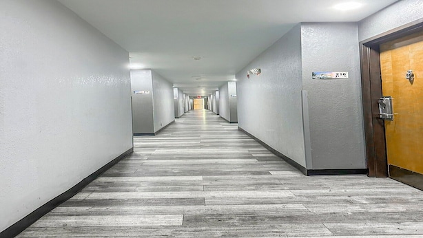 Un long couloir étroit, doté d’un plancher en bois, de murs blancs et de portes de part et d’autre.