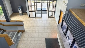 Un hall d’hôtel doté d’une porte tournante, d’un distributeur automatique de billets et d’un escalier menant à un autre étage.