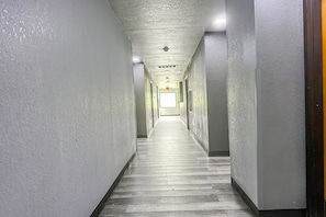 A long, narrow hallway with white walls and a wooden floor, leading to a bright room at the end.