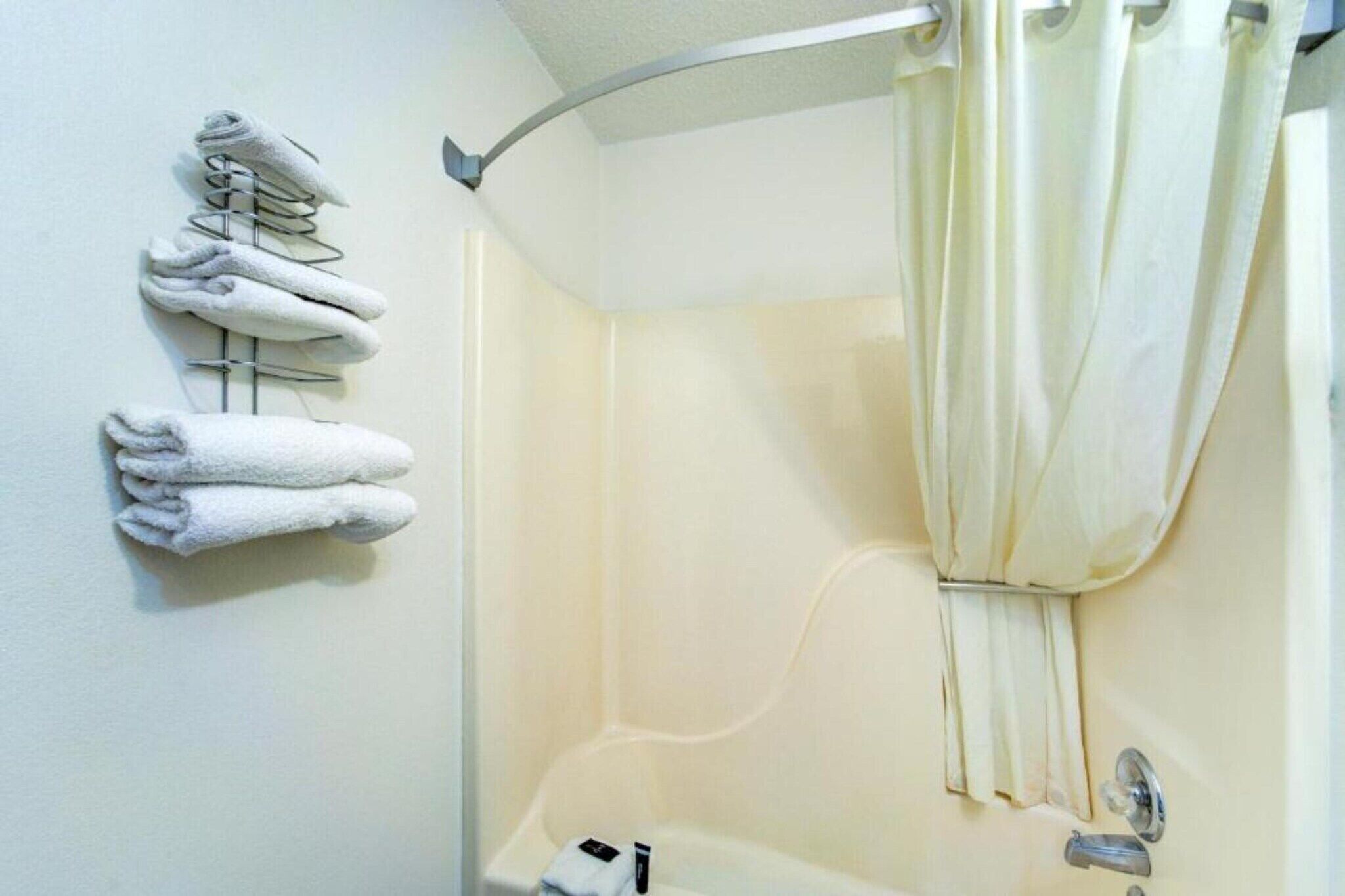 A bathroom with a shower, a towel rack with folded towels, and a shower curtain.