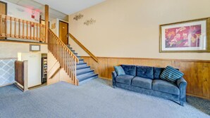 A staircase with wooden railings, a blue carpeted floor, a gray sofa with pillows, and a framed picture on the wall.