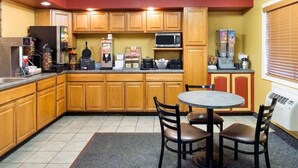 A compact kitchen with wooden cabinets, a microwave, coffee machines, and a small dining table with chairs.