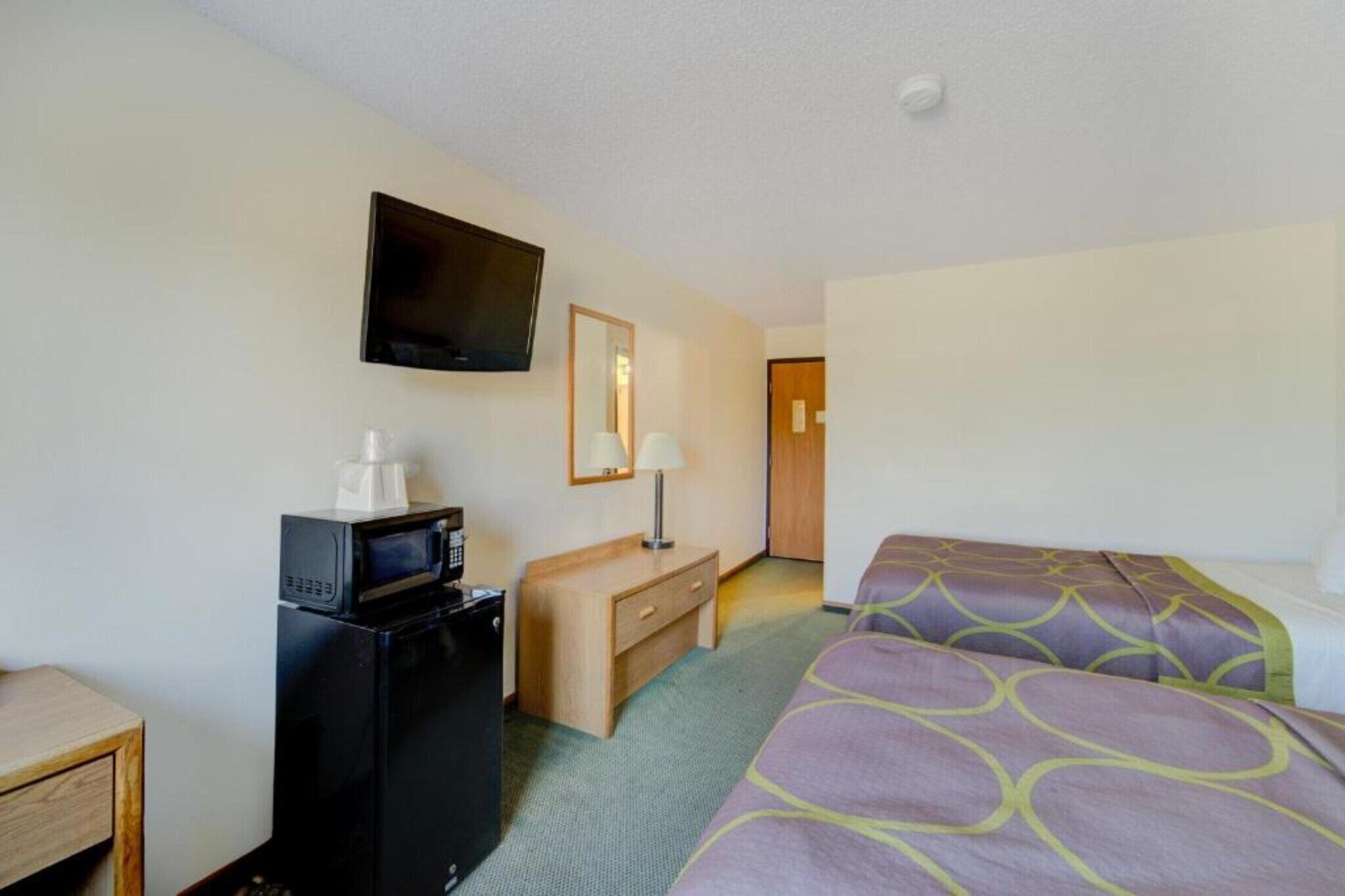 Une chambre d’hôtel comprenant un lit, un bureau avec un micro-ondes, une télévision et un miroir.