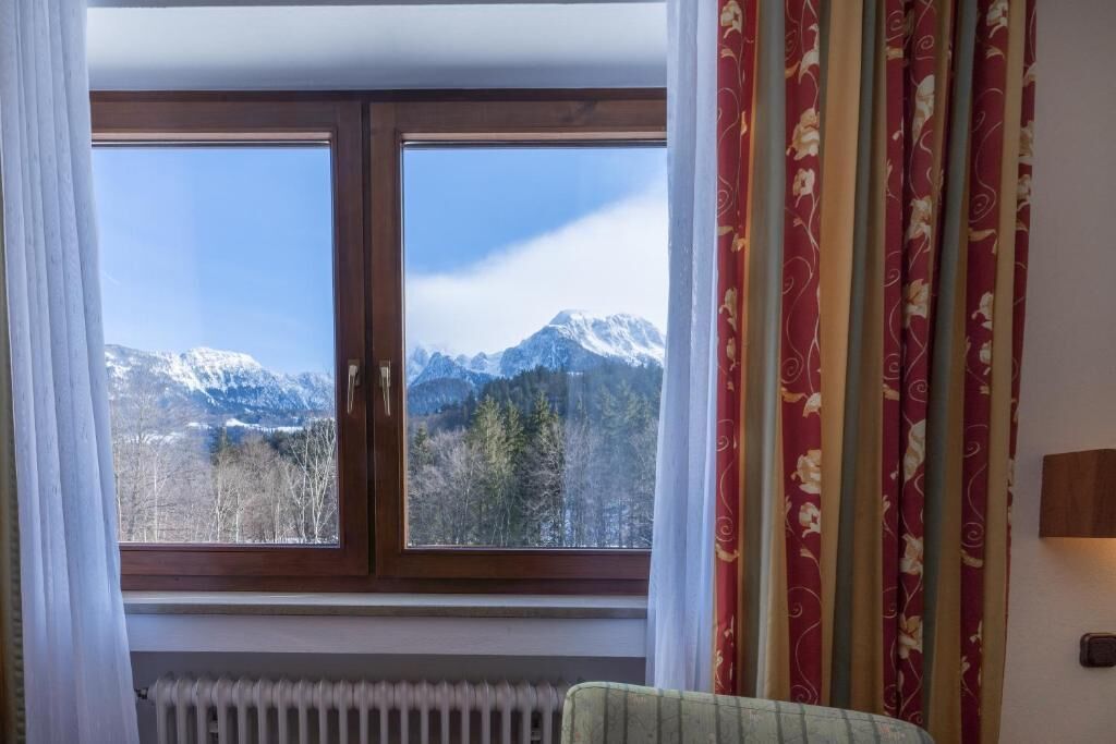 Ein Zimmer mit einem großen Fenster, einem Heizkörper darunter und einem Vorhang mit einem Blumenmuster.