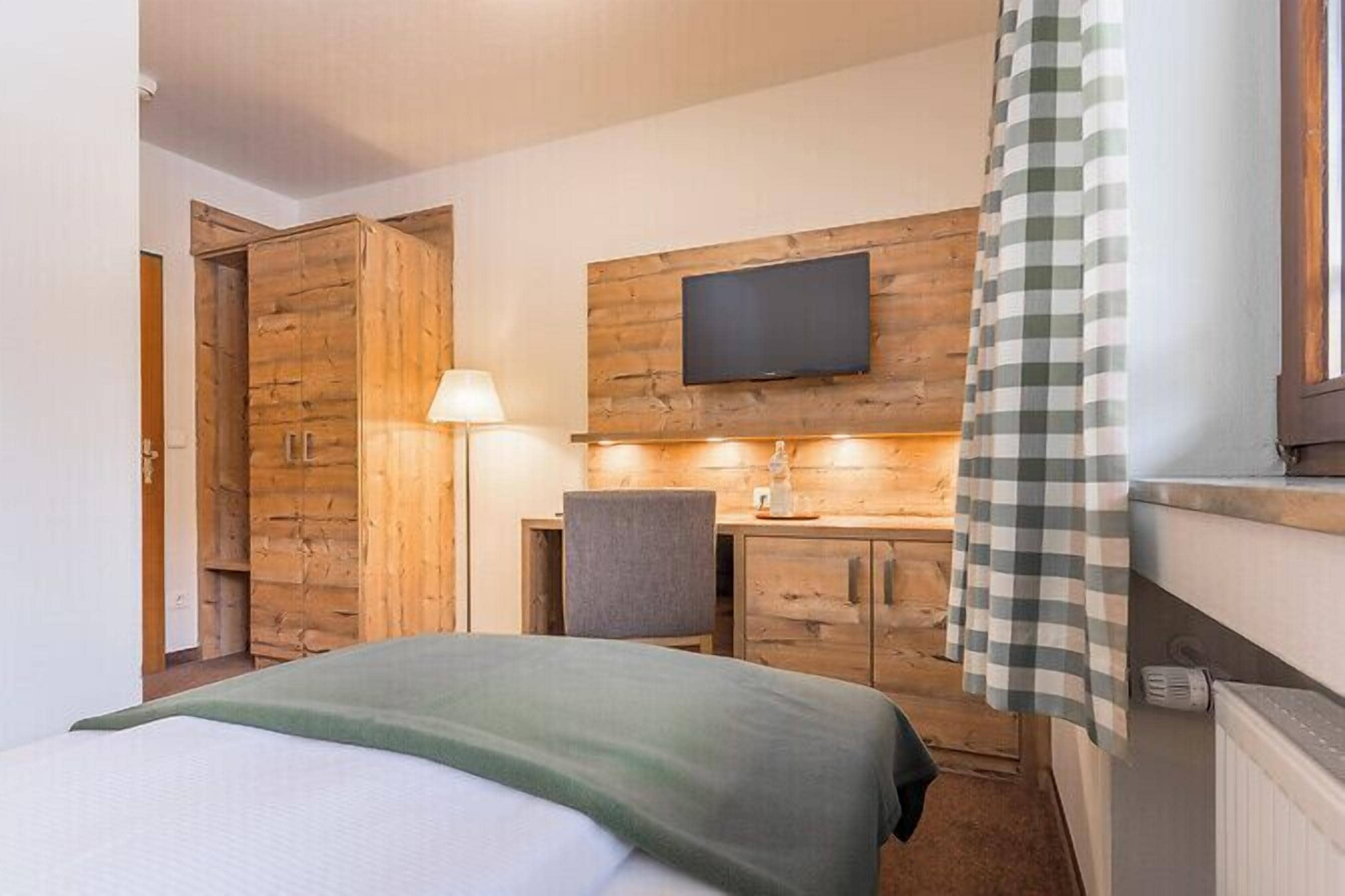 Une chambre d’hôtel comprenant un lit, un bureau avec une chaise, un téléviseur fixé au mur et une fenêtre avec un rideau.
