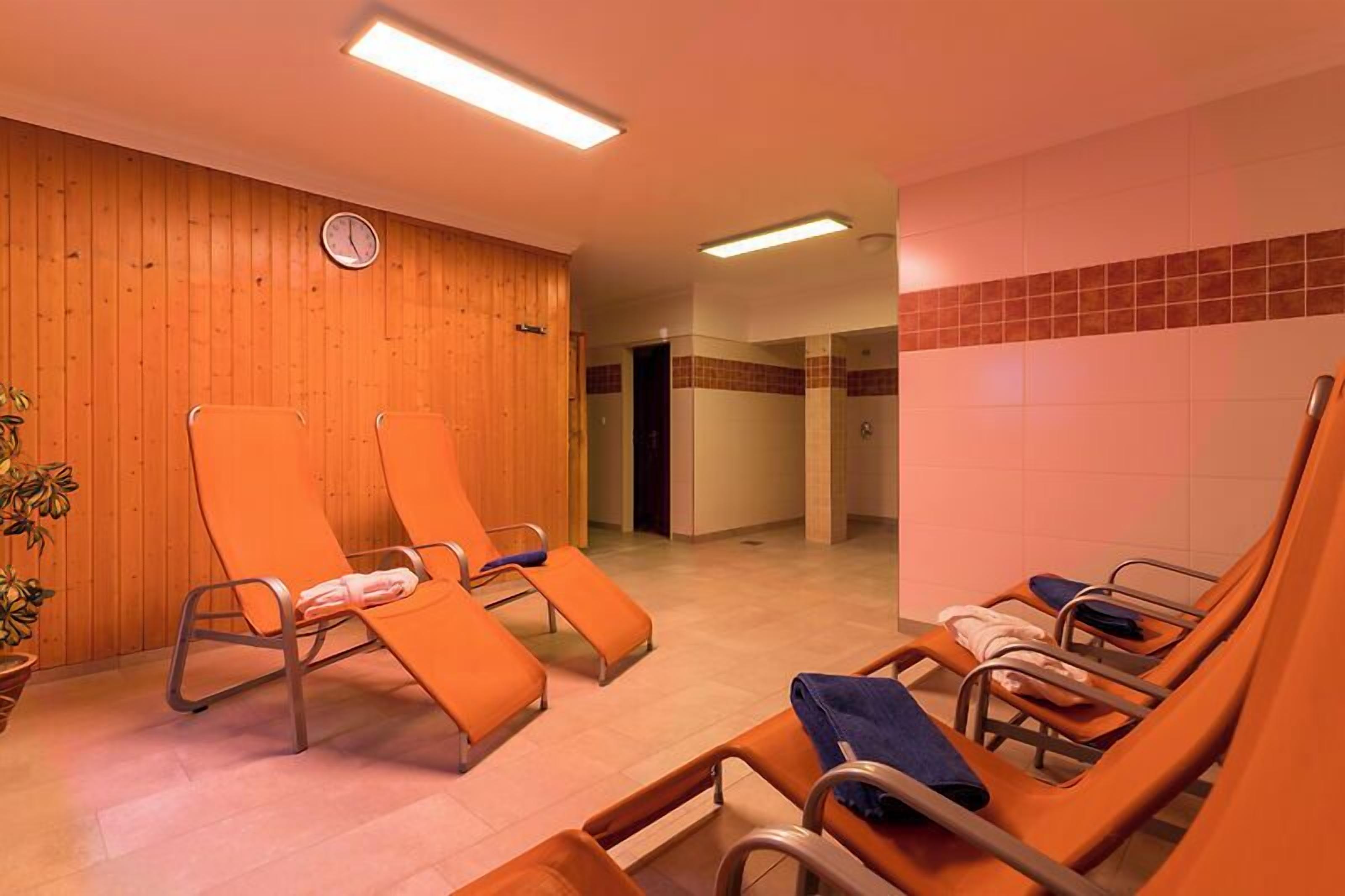 A room with wooden panel walls, a clock, and several orange lounge chairs with metal frames.