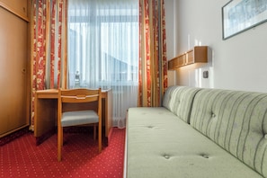 A room with a wooden desk, a chair, a sofa, and a window with curtains.