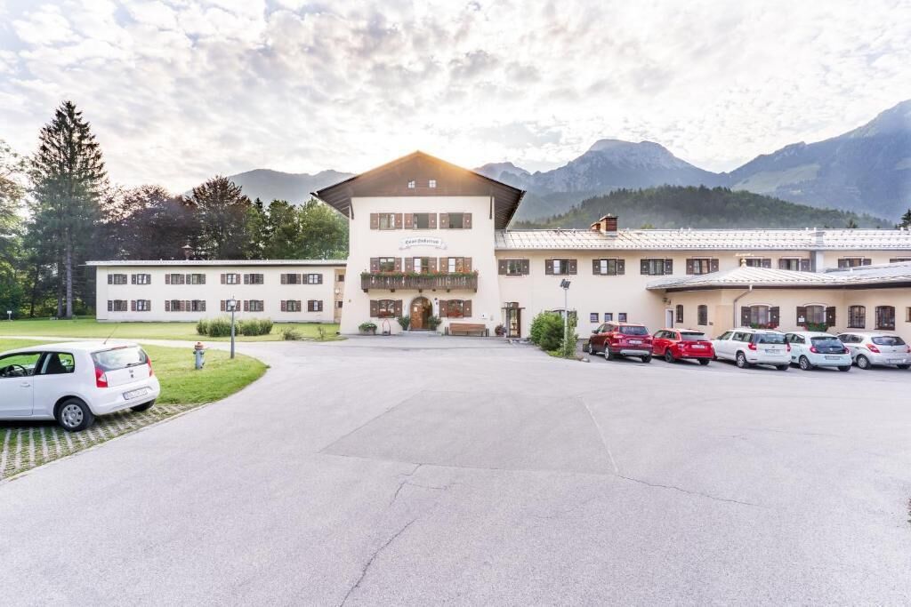 Et hotel med en hovedbygning, parkeringsplads og bjerge i baggrunden.
