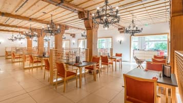 Un vaste espace dédié à la salle à manger, avec des tables et des chaises en bois, des lustres et de grandes fenêtres.