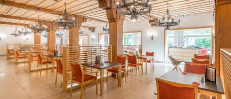 Un comedor espacioso con mesas y sillas de madera, candelabros y ventanas grandes.