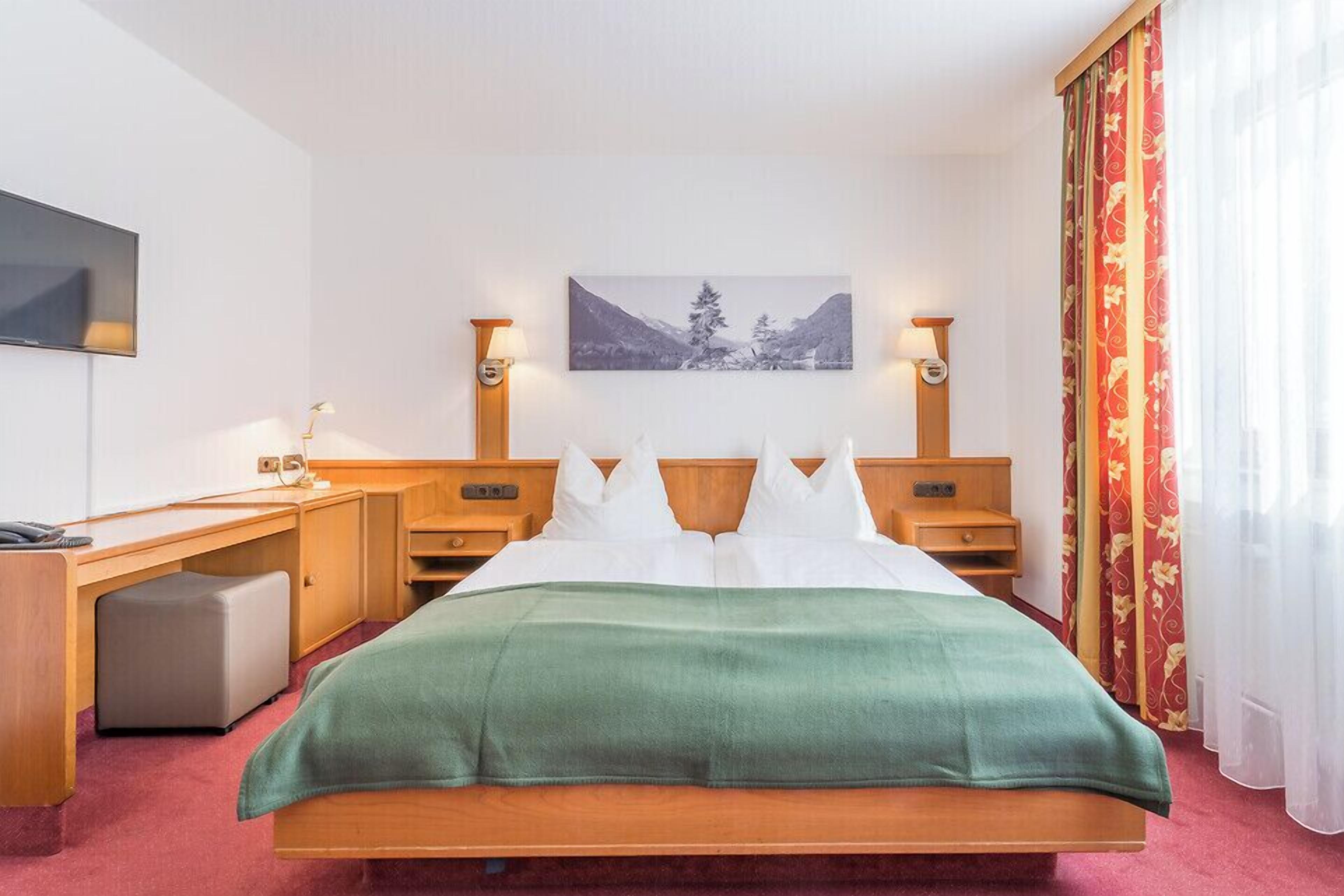 A hotel room with a bed, a desk, a chair, a television, and a painting on the wall.
