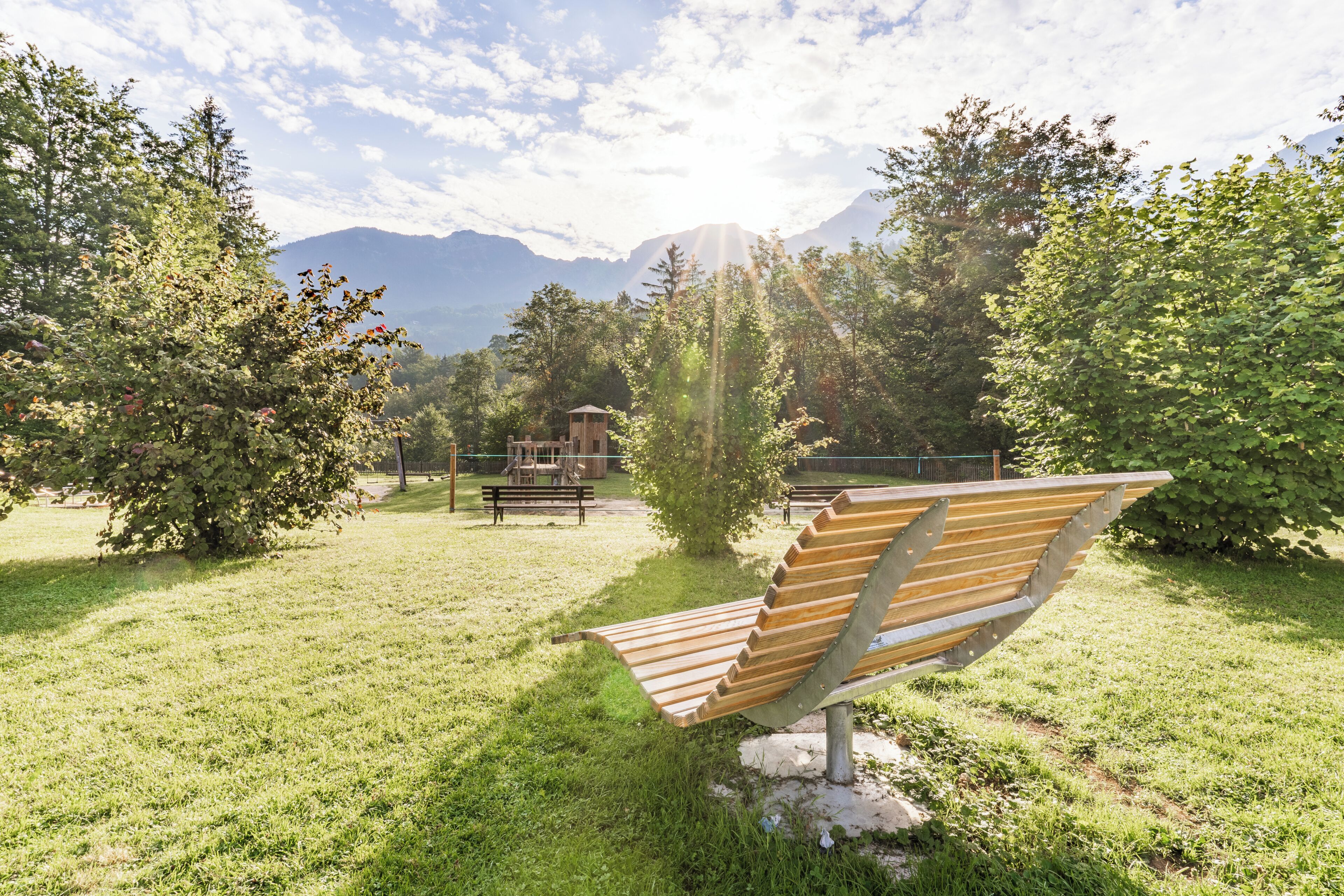 A park with a wooden bench, a playground, and a mountain backdrop.