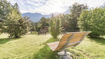 A park with a wooden bench, a playground, and a mountain backdrop.