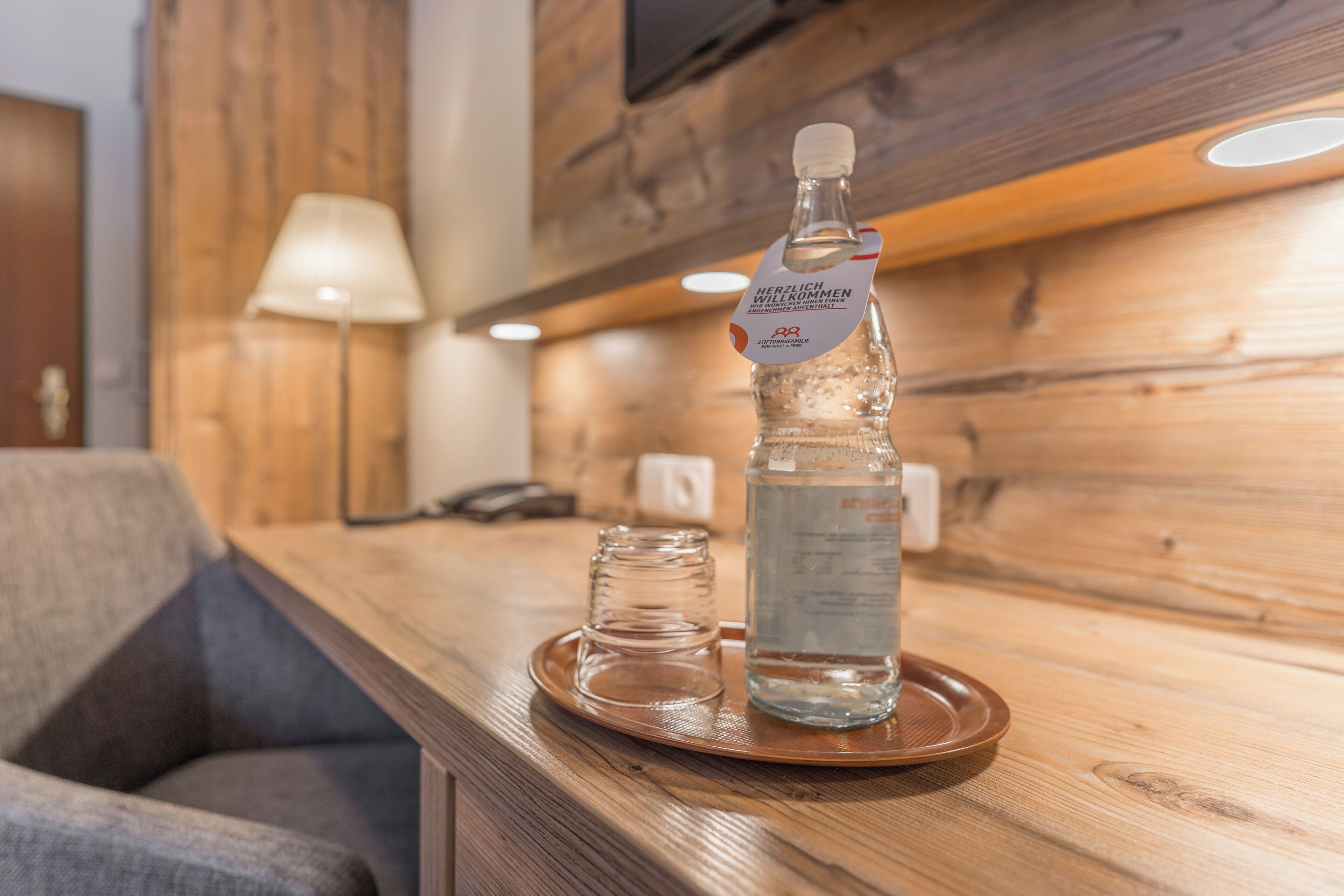 Eine Holztresore mit einer Wasserflasche, einem Glas und einem kleinen Glaskrug auf einer Ablagefläche.