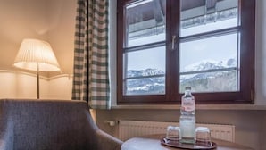 Une pièce avec une chaise, une table sur laquelle se trouvent une bouteille et des verres, une fenêtre donnant sur des montagnes enneigées et une lampe.