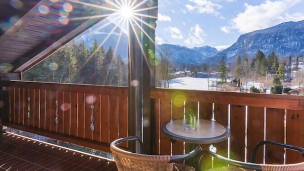 Une terrasse en bois avec une table et des chaises, offrant une vue sur un paysage montagneux avec un lac.