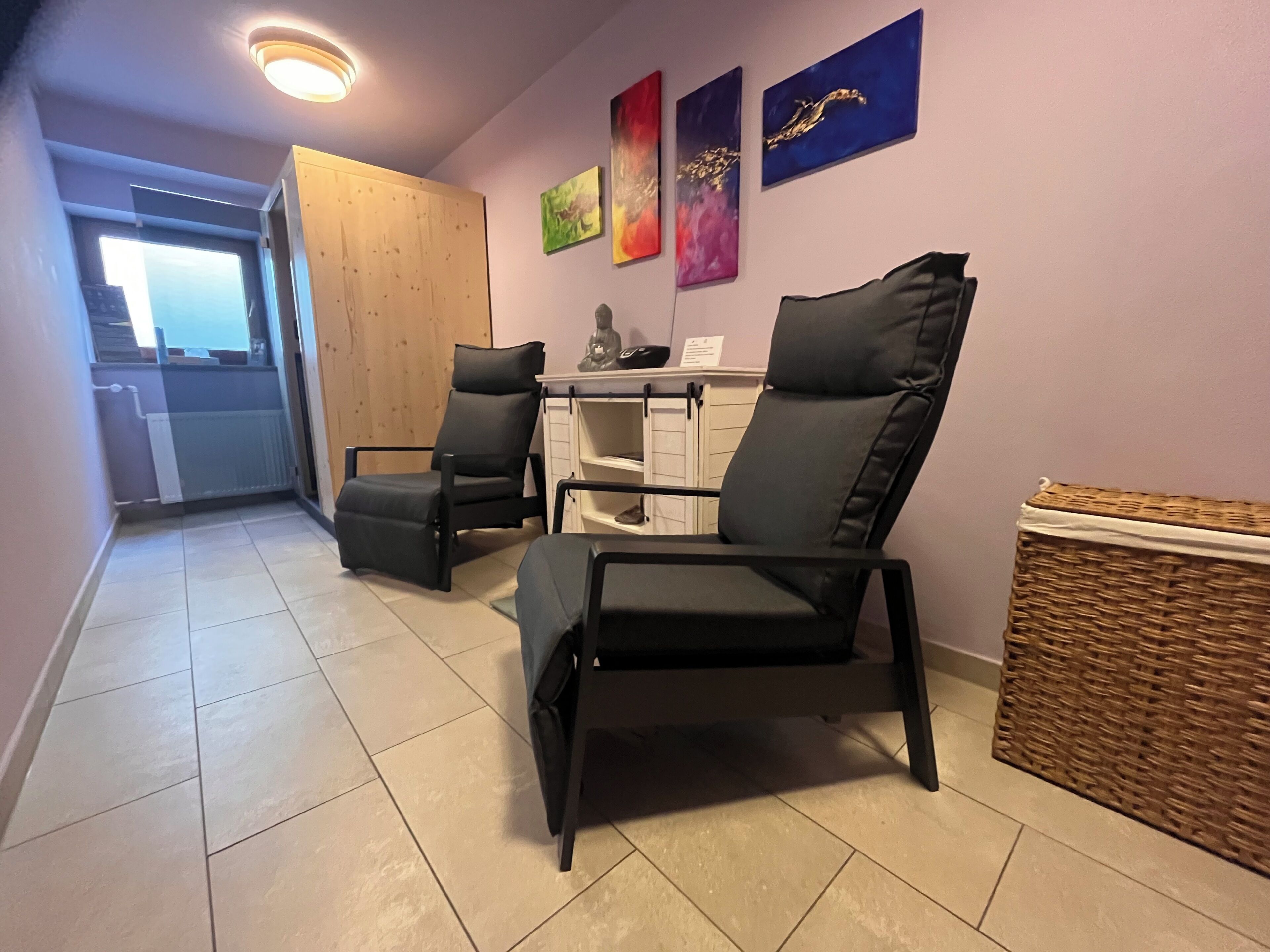 Una habitación con dos sillas negras, un armario de madera y una cesta de mimbre.