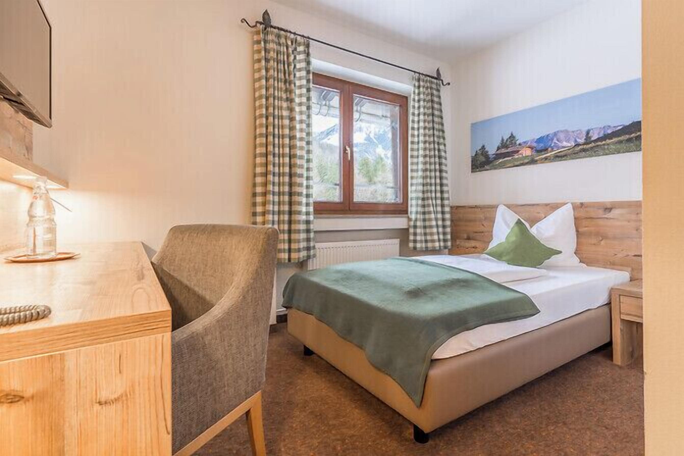 Ein Schlafzimmer mit Bett, Stuhl, Schreibtisch und einem Fenster mit Vorhängen.