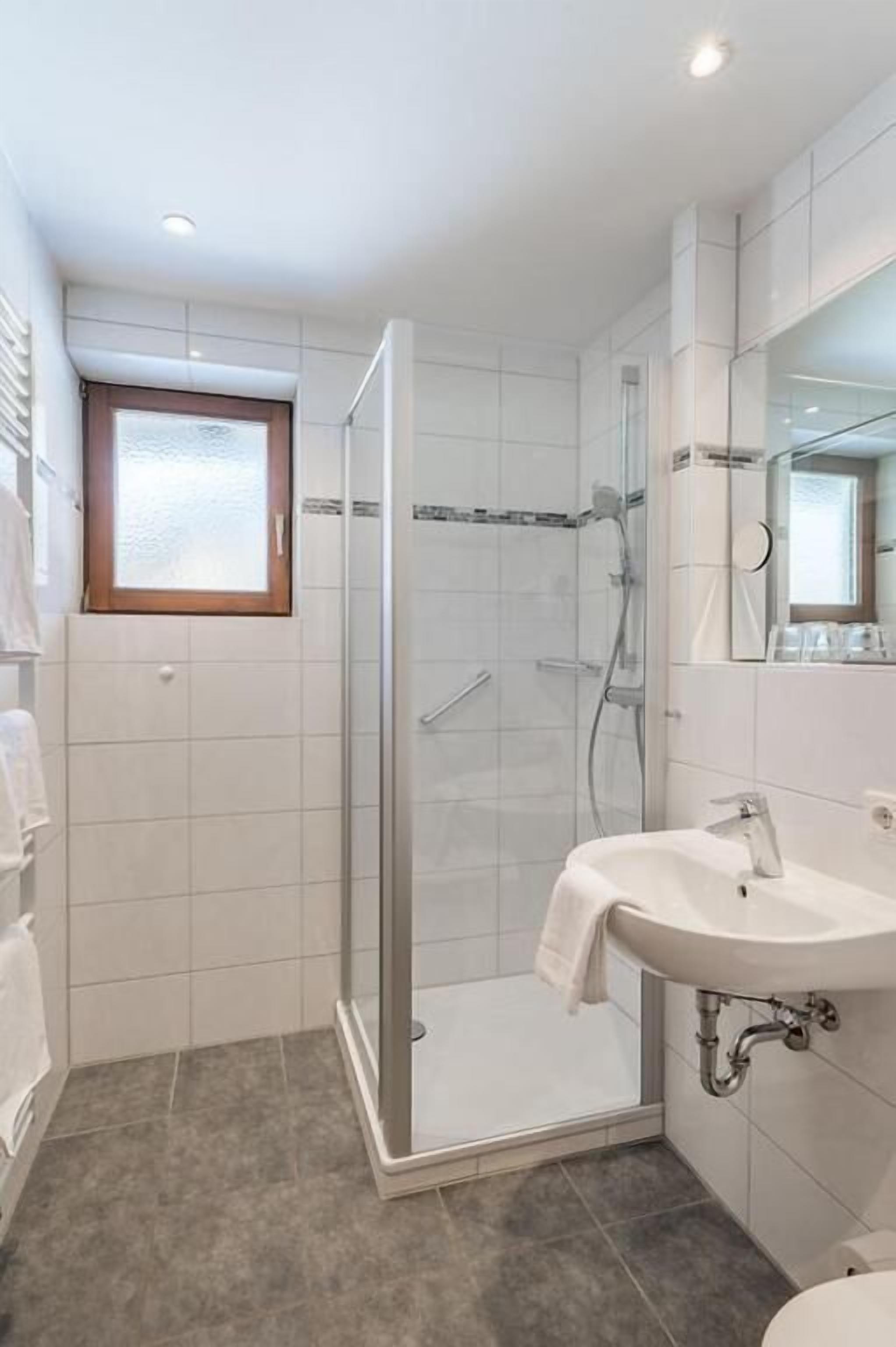 Een badkamer met een douche met glazen wand, een wit wastafelmeubel en een spiegel.