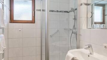 Een badkamer met een douche met glazen wand, een wit wastafelmeubel en een spiegel.