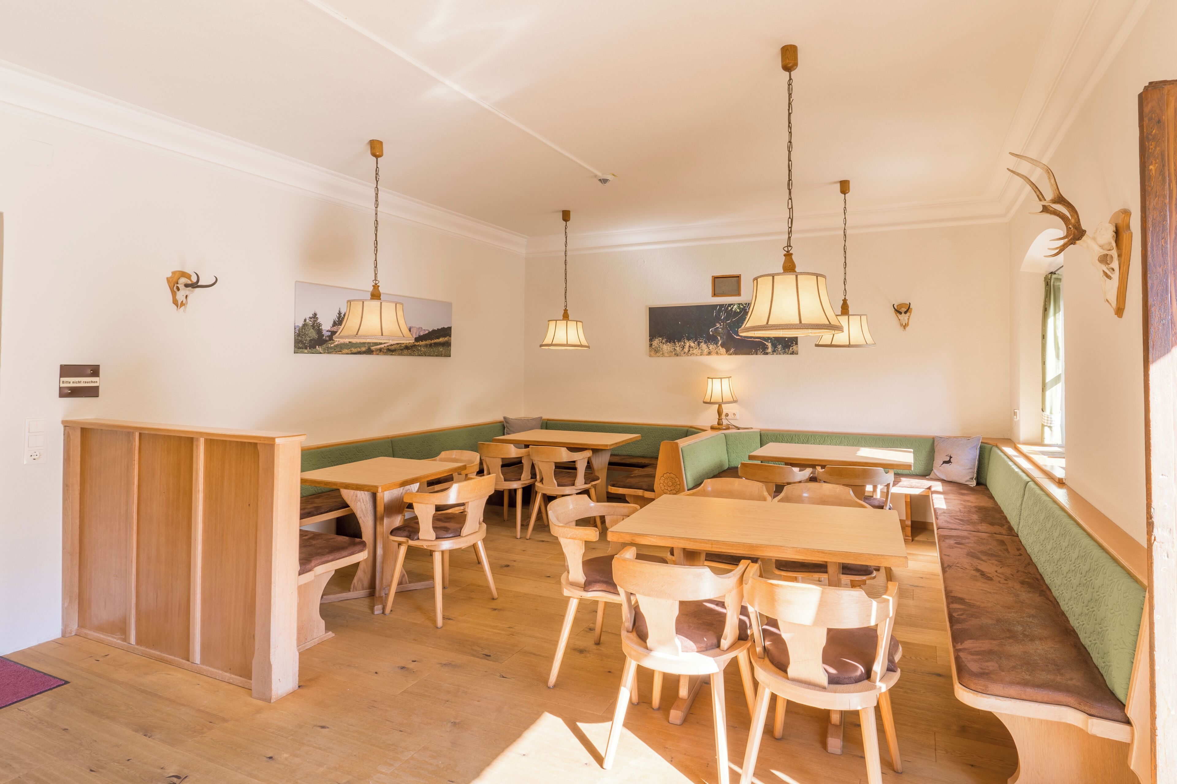 Un restaurante con mesas y sillas de madera, una zona de asientos con bancos verdes e iluminación colgante.