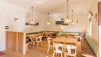Un restaurante con mesas y sillas de madera, una zona de asientos con bancos verdes e iluminación colgante.