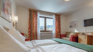 Une chambre d’hôtel avec deux lits, un bureau, une chaise, une télévision et une fenêtre avec des rideaux.
