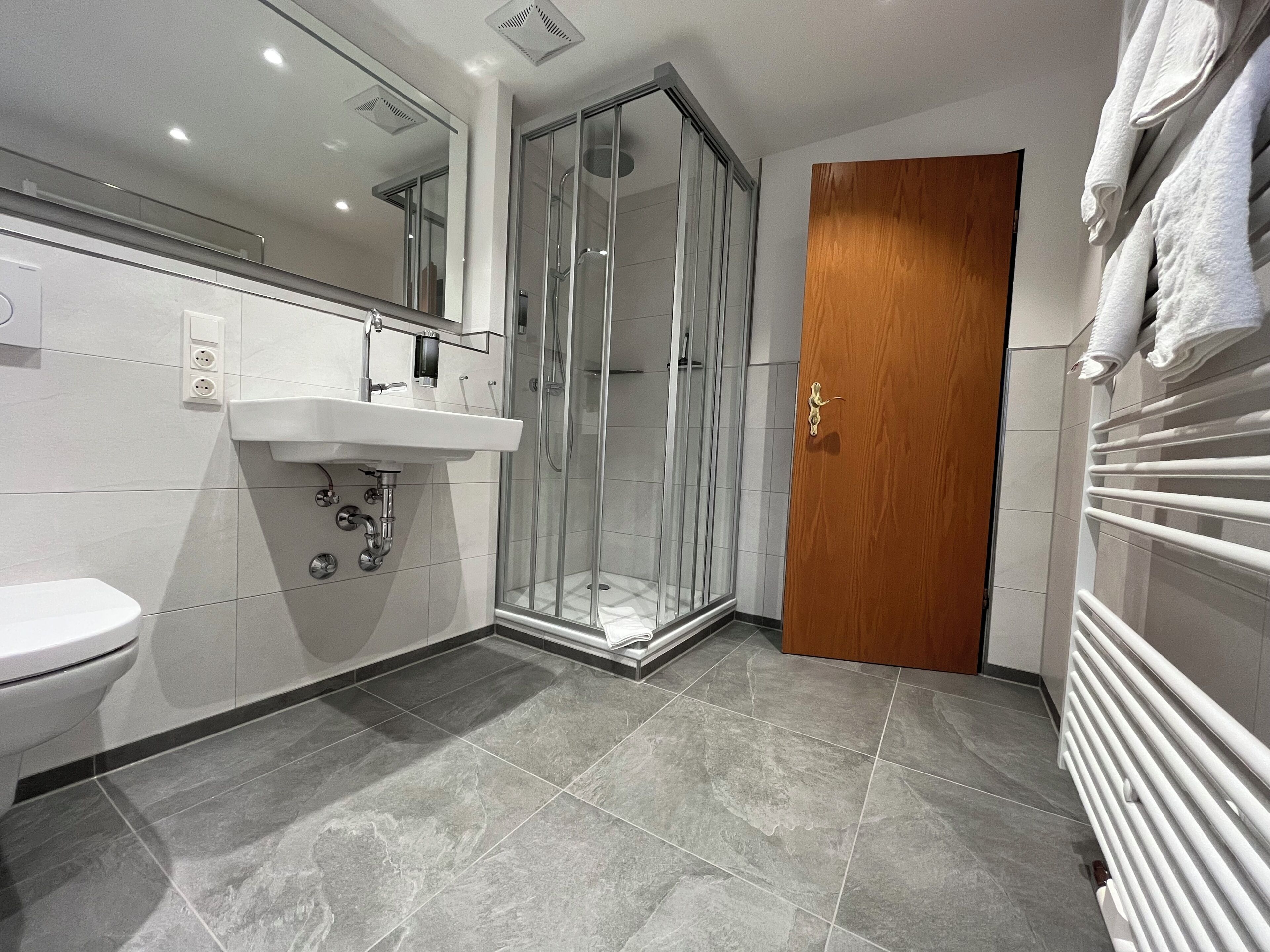 A modern bathroom with a glass-enclosed shower, a white sink, and a wooden door.