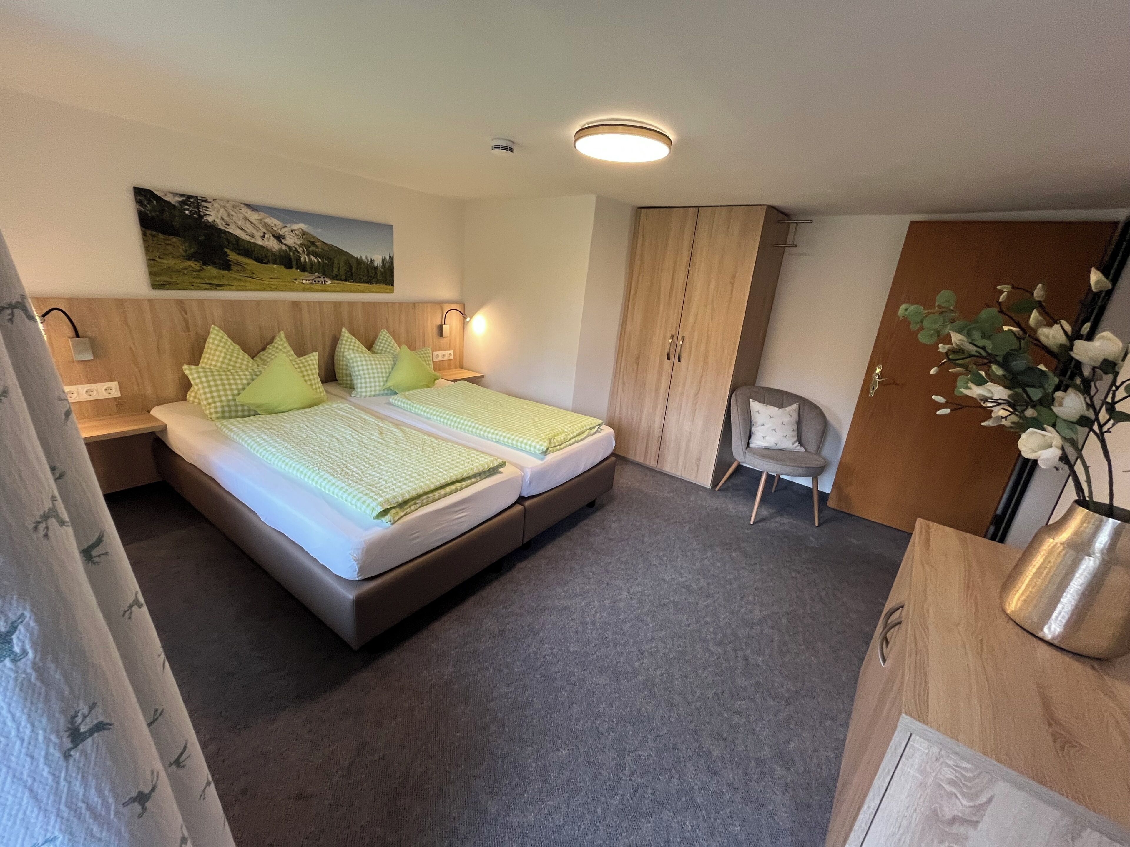 Hotellihuone, jossa on kaksi sänkyä, puinen vaatekaappi, tuoli ja taulu seinällä.