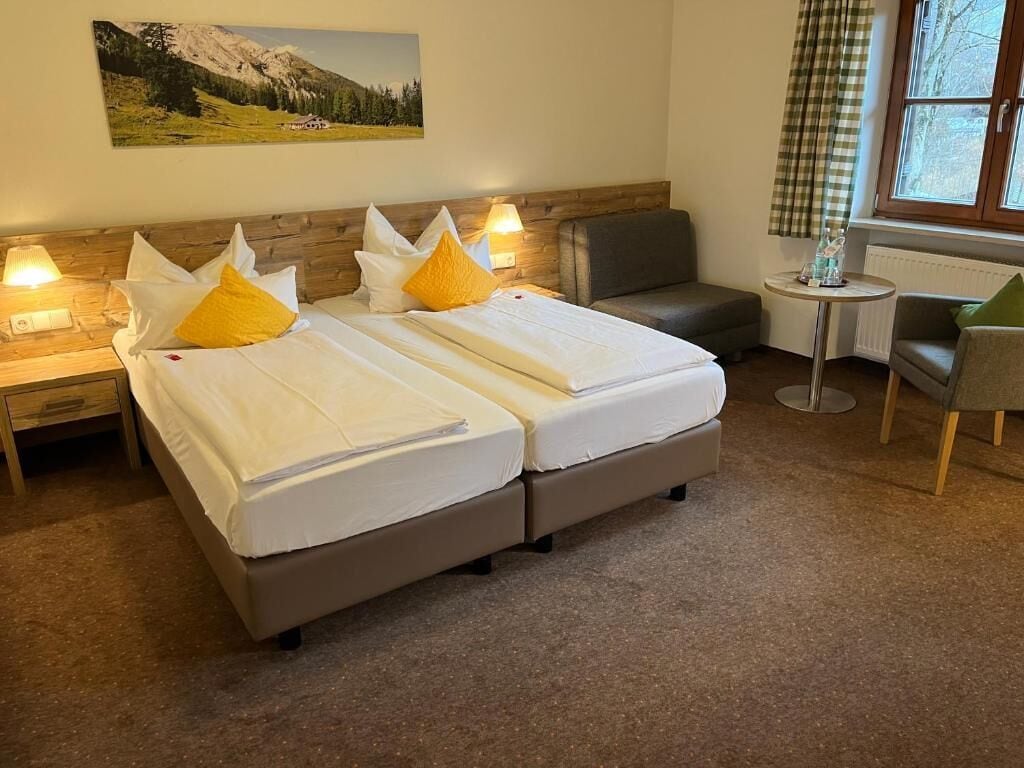 Ein Hotelzimmer mit zwei Betten, einem kleinen Tisch, einem Stuhl und einem Fenster mit Vorhängen.